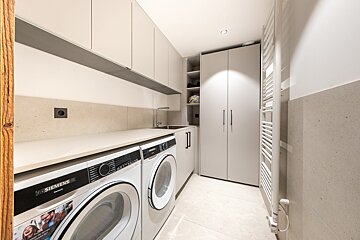 Modern minimalist laundry room featuring white Siemens appliances, light grey cabinets, a sink, and a tall wardrobe.