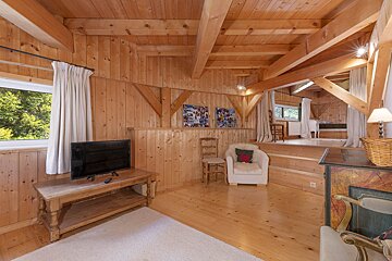 Cozy rustic cabin interior with light wood walls and ceilings, featuring a TV, armchairs, and exposed wooden beams.