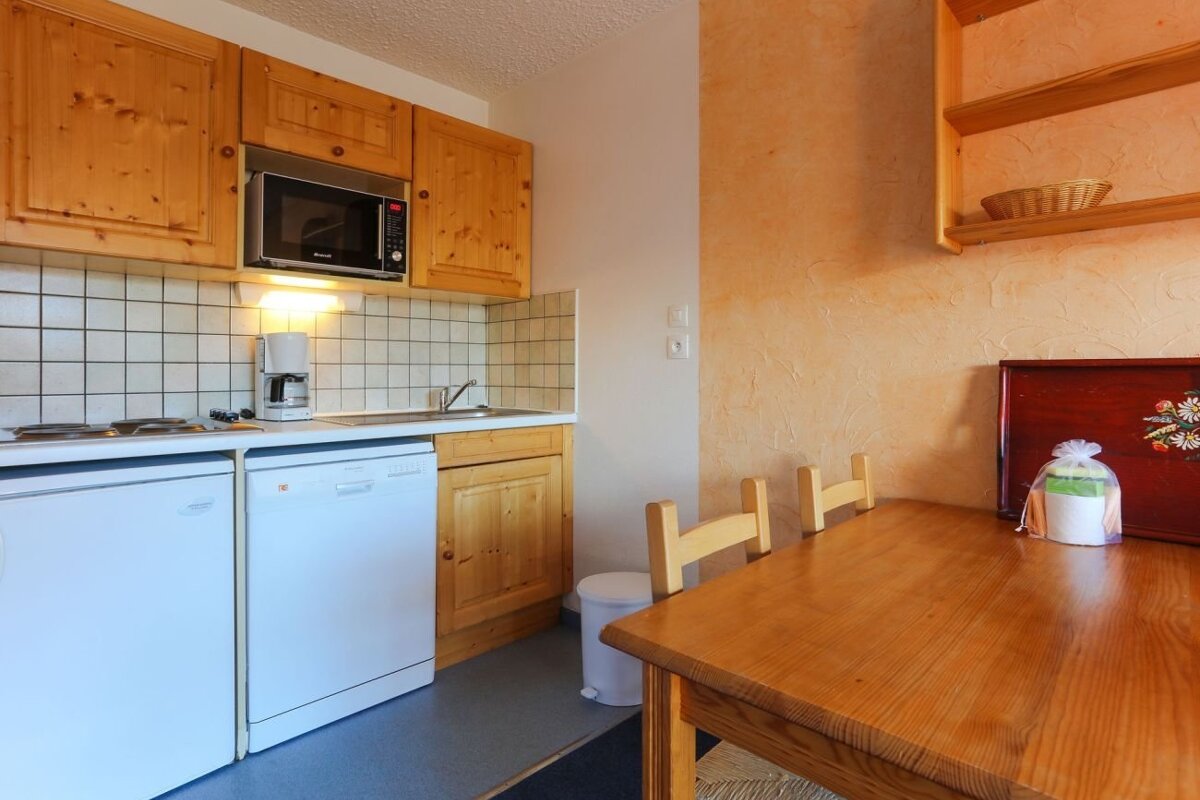 A cozy kitchen featuring light wood cabinets, white appliances, and a wooden dining table set against a warm, peach-colored wall.