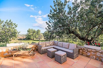 A patio with a couch and ottoman under a tree