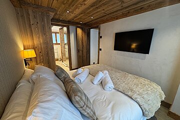 Cozy chalet bedroom with wood-paneled ceilings, a neat bed with rolled towels, wall-mounted TV, and an en-suite bathroom.
