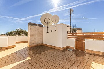 Sunny tiled rooftop terrace with satellite dishes, antennae, and contrails across a bright blue sky.
