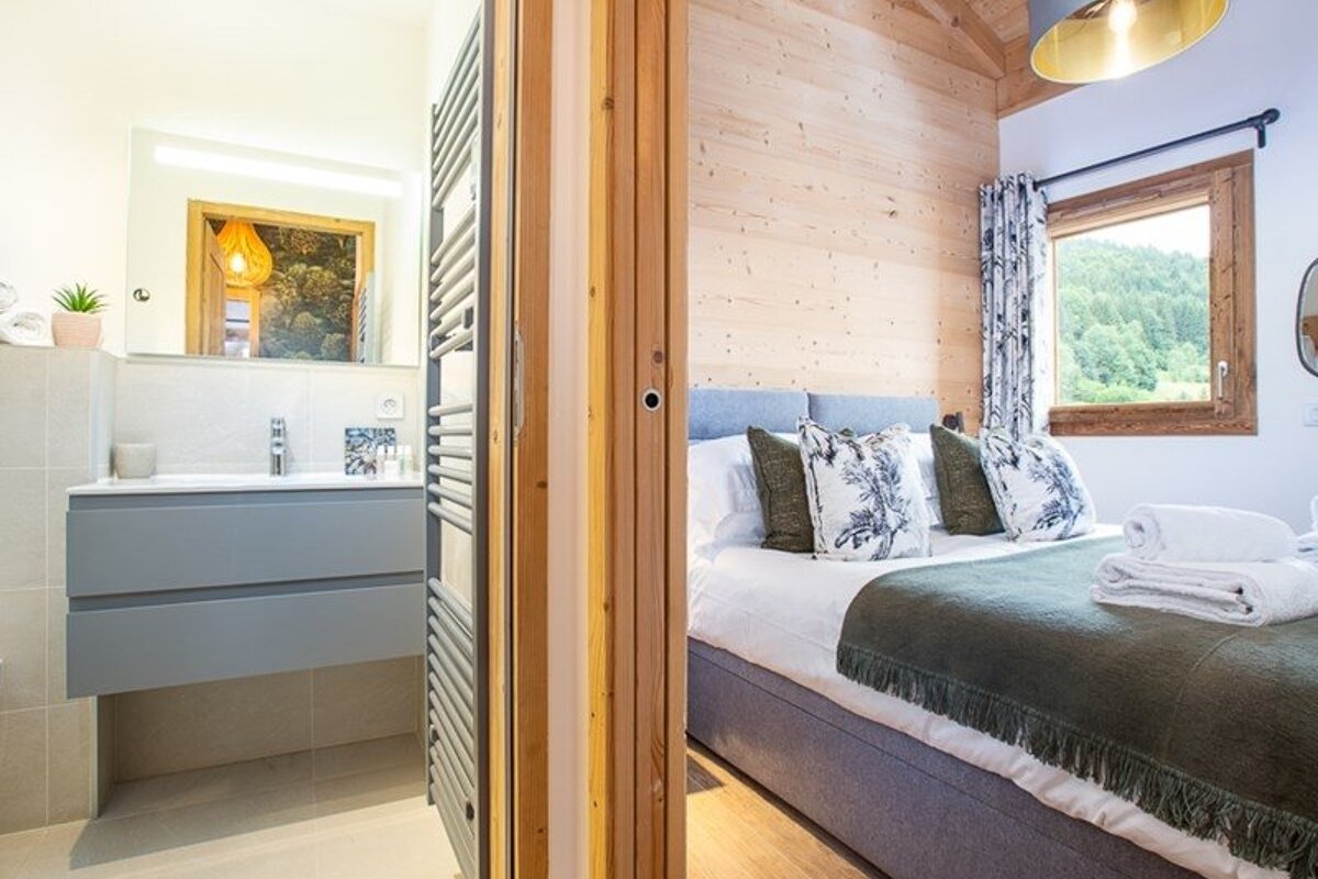 A wooden sliding door separates a modern bathroom with a grey vanity from a cozy cabin-style bedroom.