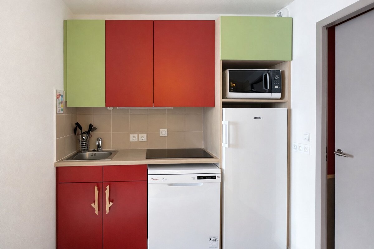 A small, colorful kitchen with red & green cabinets, sink, stovetop, microwave, fridge, & dishwasher.