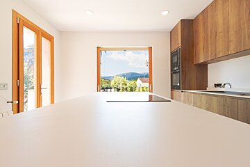 Bright, modern kitchen with a spacious white island, wooden cabinets, and large open doors offering a scenic view of mountains, trees, and blue sky.