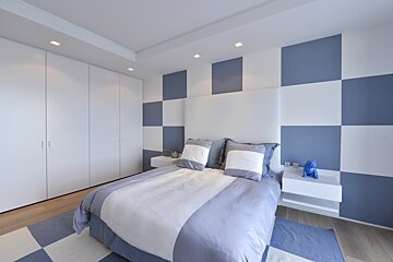 Stylish bedroom with a bold blue and white checkerboard wall, coordinated bed, white headboard, and sleek white wardrobes.