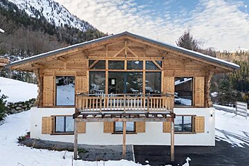 A two-story wooden chalet with a balcony, surrounded by a snowy mountain landscape.
