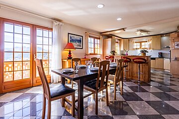 Bright dining and kitchen area featuring wooden furniture, checkered floors, and French doors opening to a scenic mountain view.