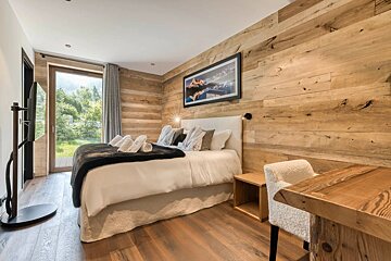 Cozy bedroom with wooden walls and floors, featuring a double bed, a white desk chair, a glass door to the outside, and a TV stand.