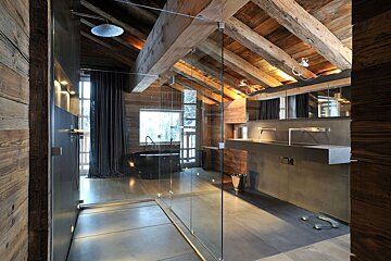 Luxurious modern-rustic bathroom with vaulted wooden ceilings, glass shower, black tub, and sleek double sinks.