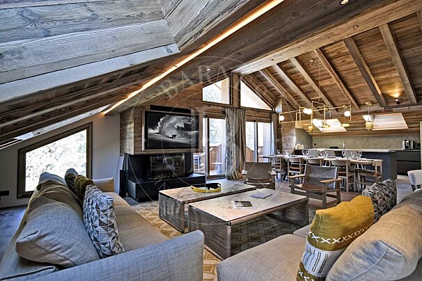A luxurious, open-plan chalet living space featuring vaulted wooden ceilings, a modern fireplace, dining area, and large windows with outdoor views.