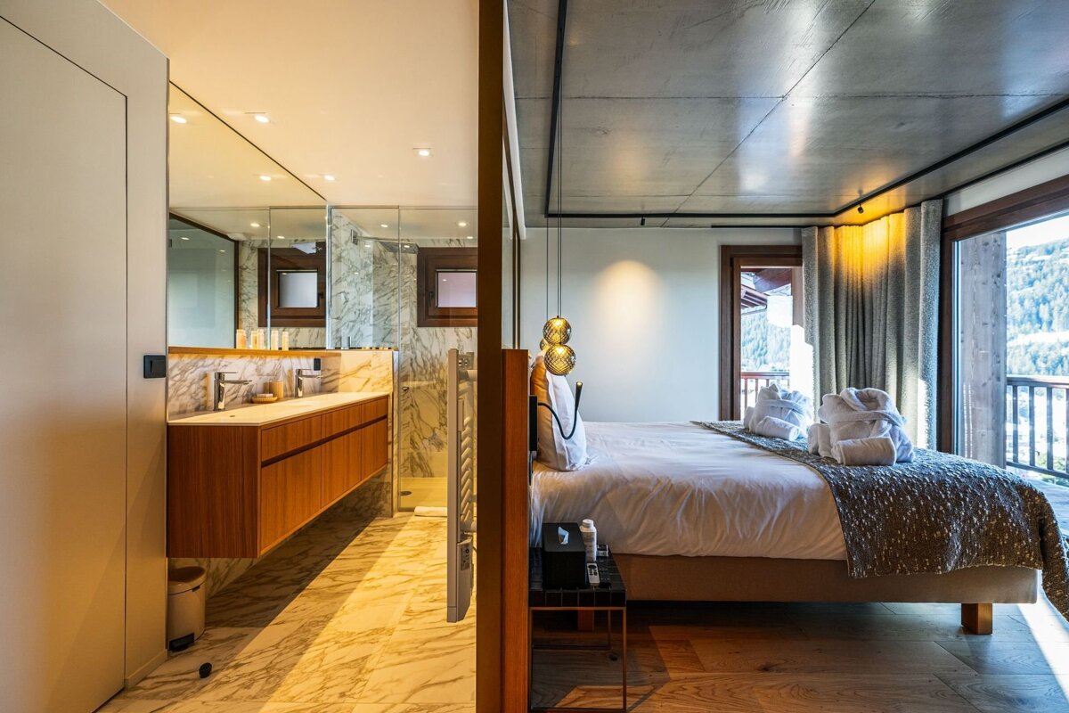 Modern bedroom with an en-suite bathroom, featuring a double vanity, and a mountain view from a balcony.