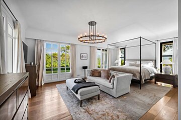 Elegant bedroom featuring a black canopy bed, a light grey sofa, French doors, hardwood floors, and a modern circular chandelier.