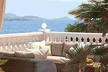 A balcony with a couch and palm trees overlooking the ocean