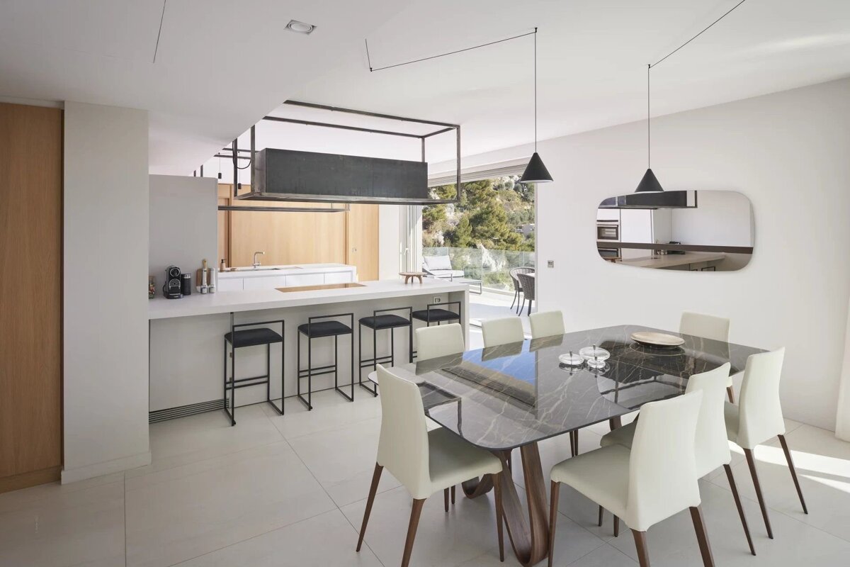 Modern dining room and kitchen with a marble table, white chairs, and a long island with bar stools.