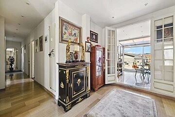 Elegant interior with a black and gold cabinet, wooden floors, and French doors opening to a sunny terrace with city views.