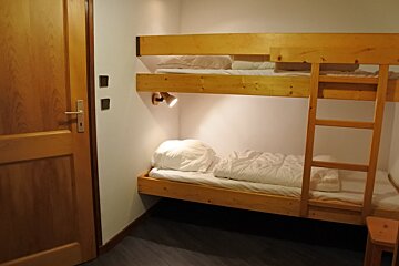 A wooden bunk bed with white sheets and a ladder
