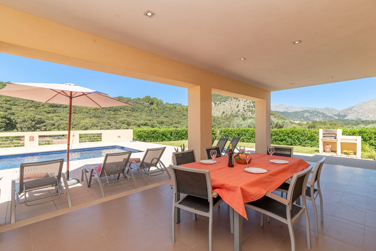 A table and chairs on a patio with an umbrella and mountains in the background