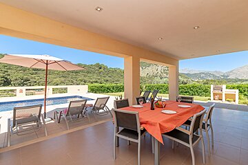 A table and chairs on a patio with an umbrella and mountains in the background