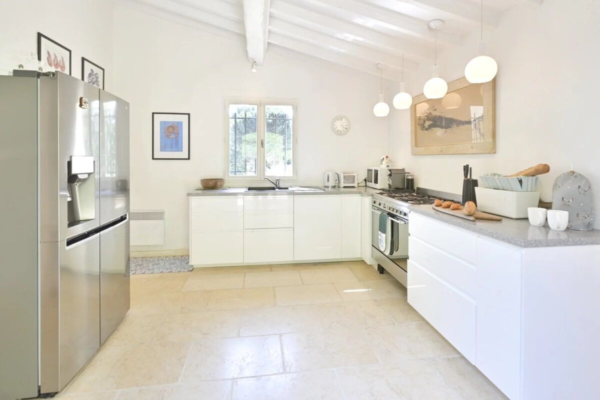 A bright, modern white kitchen with a tiled floor, stainless steel appliances, and a vaulted ceiling with exposed beams.