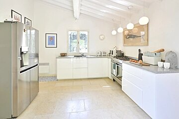 A clean, bright kitchen featuring white cabinets, light stone floor, stainless steel appliances, spherical pendant lights, and a window.