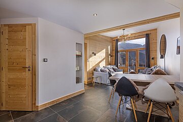 Cozy modern chalet interior featuring a dining area, wooden-paneled living room, and large windows with mountain views.