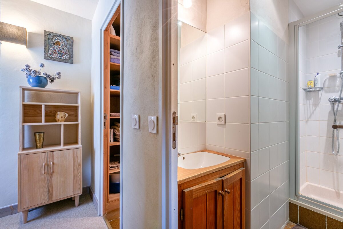 A view of a rustic bathroom with a wooden vanity and shower, adjacent to a room with a wooden cabinet.