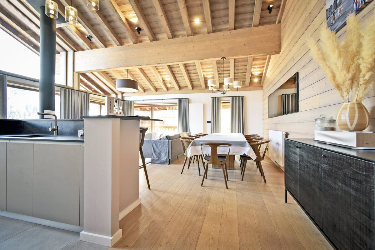 Bright, open-plan living space with a modern kitchen, dining area, and lounge. Features a vaulted wooden ceiling, light wood floors, and natural decor.