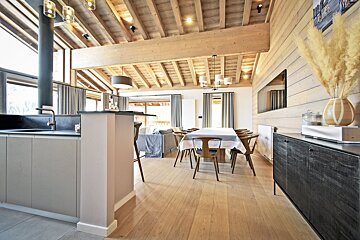 Bright, open-plan chalet interior with a modern kitchen, dining area, and living space, all under a beautiful vaulted wooden ceiling.