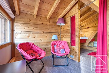 Cozy wooden cabin interior featuring two pink folding chairs, standing lamps, and rustic wood-paneled walls and ceiling.