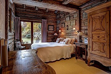 A warm, rustic log cabin bedroom, rich with wooden textures, a cozy bed, and a large window inviting nature inside.