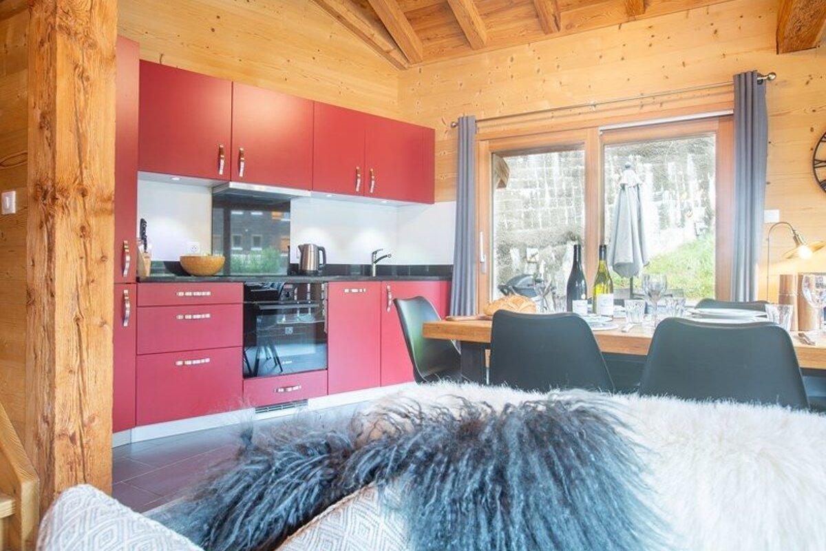Cozy wooden cabin interior featuring a red kitchen, dining area, and a furry blanket in the foreground.