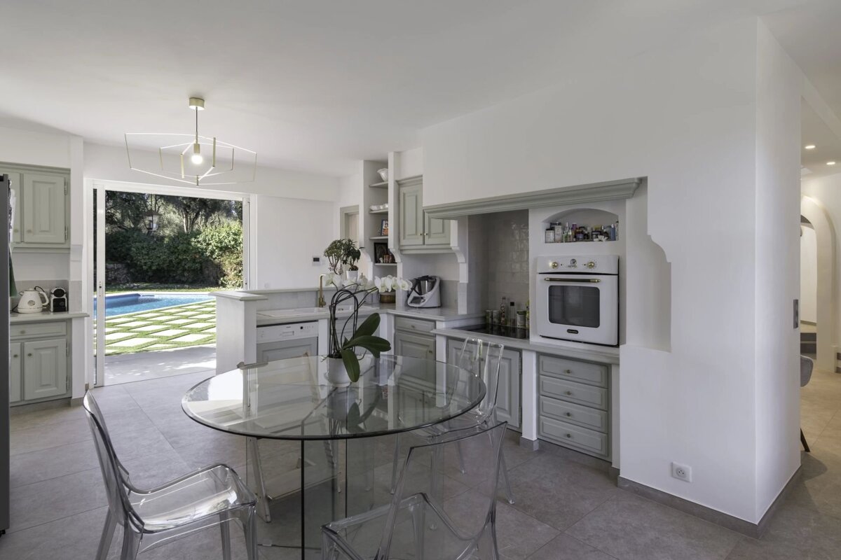 Bright, modern kitchen with light green cabinets, a glass dining set, and sliding doors opening to a patio with a swimming pool.
