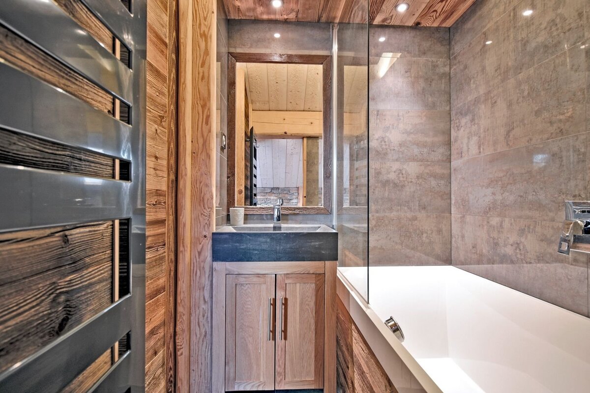 Modern rustic bathroom with wood paneling, a stone sink vanity, a mirror, and a glass-enclosed bathtub.