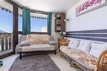 A cozy living space features two couches, one rattan, teal curtains, and a large window with a snowy mountain view. A pink flower painting hangs above.