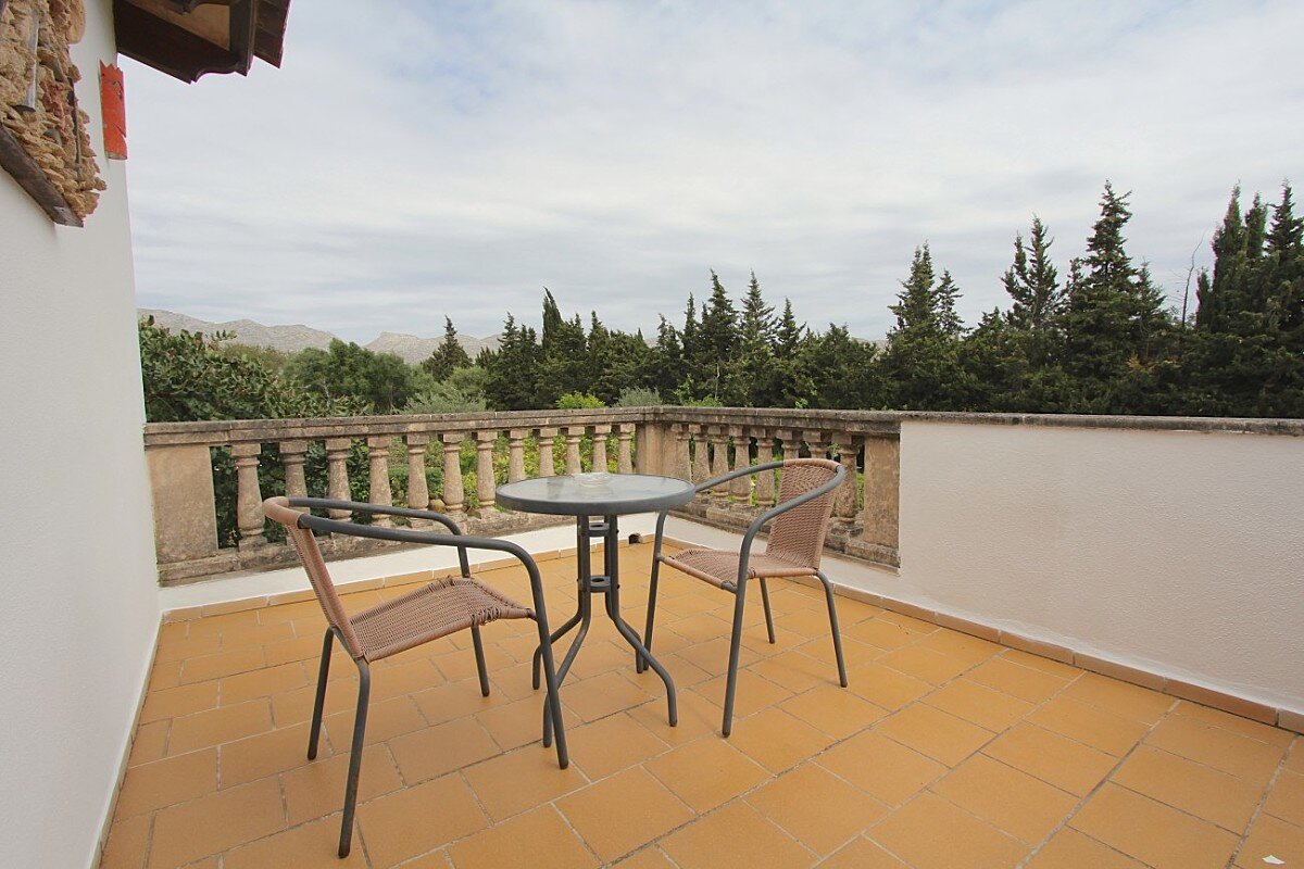 A balcony with two chairs and a table with trees in the background