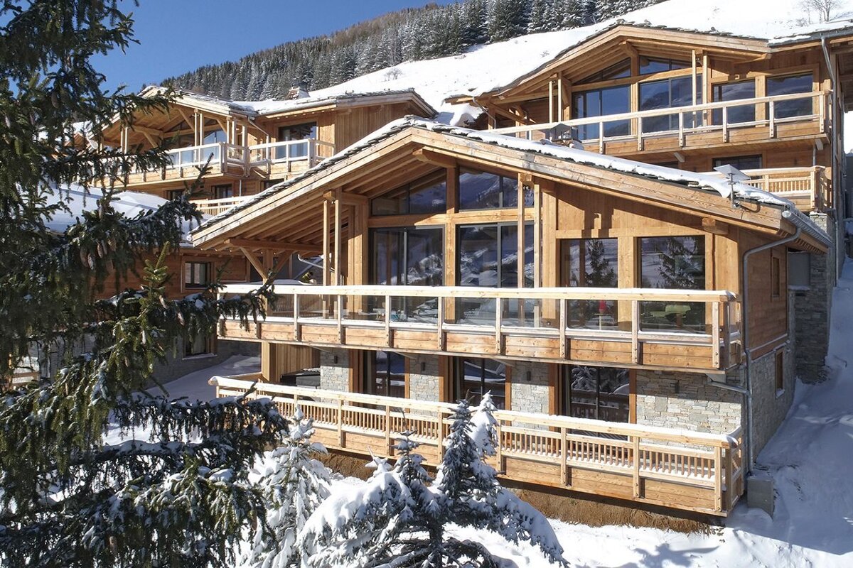 A large wooden house with a lot of windows is surrounded by snow