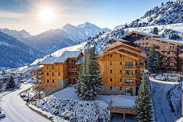 Wooden ski chalets in a snow-covered mountain resort under a bright, sunny winter sky.