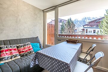 Cozy room with a sofa, dining table, and large window overlooking a mountain town with trees and buildings.