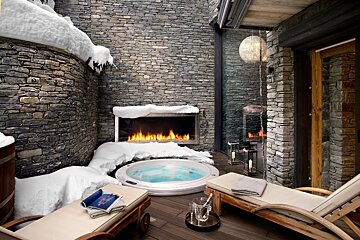 A hot tub is surrounded by snow and a stone wall