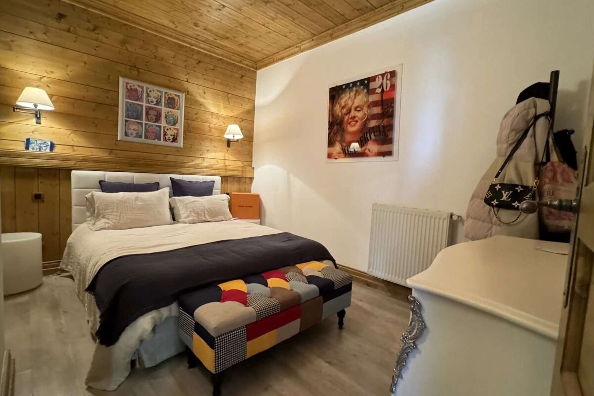A cozy bedroom with wood-paneled walls, a bed, a colorful patchwork bench, and Marilyn Monroe art on the walls.