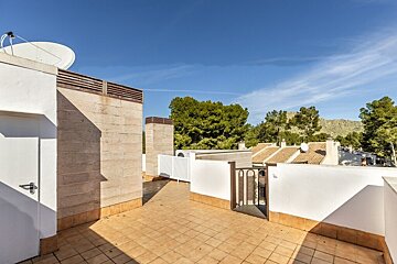 A sunny tiled rooftop terrace with views of green trees and hills under a clear blue sky.