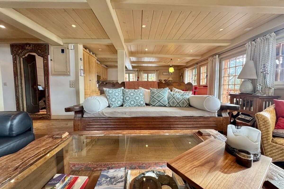 Rustic wooden living room with a daybed, patterned pillows, glass coffee table, and ornate carved doorway under a wood-paneled ceiling.