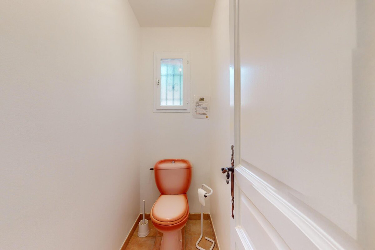 An orange toilet sits in a bathroom next to a window