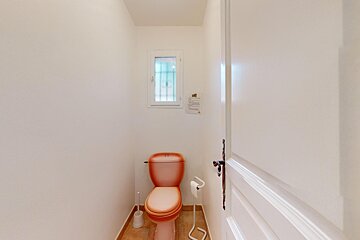 An orange toilet sits in a bathroom next to a window