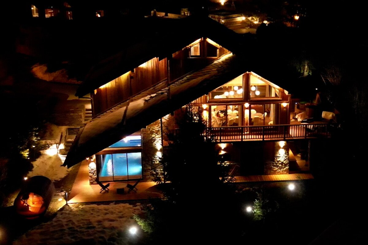 A large house with a swimming pool is lit up at night