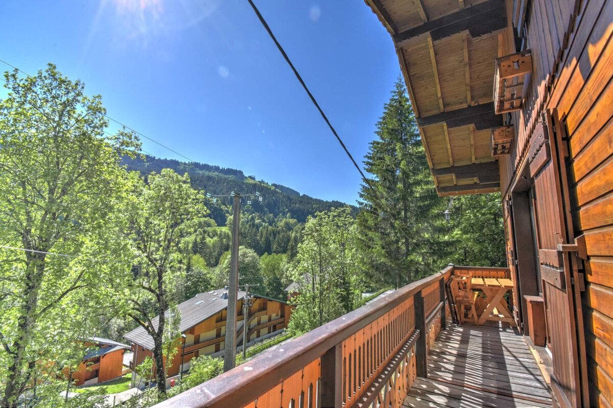 View from a wooden chalet balcony overlooking lush green mountains under a bright blue sky.