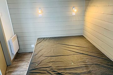 A bedroom with a mattress and two lights on the wall