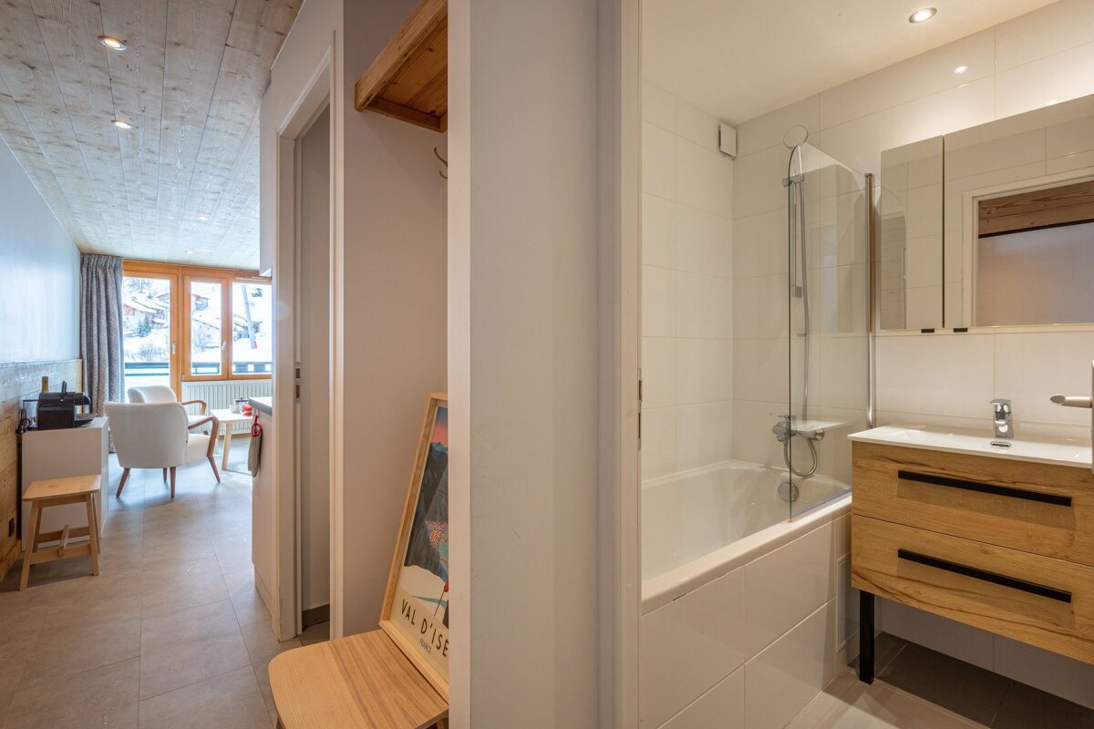 A modern apartment interior featuring a sleek bathroom with a tub, a hallway with a ski poster, and a living area with a snowy mountain view.