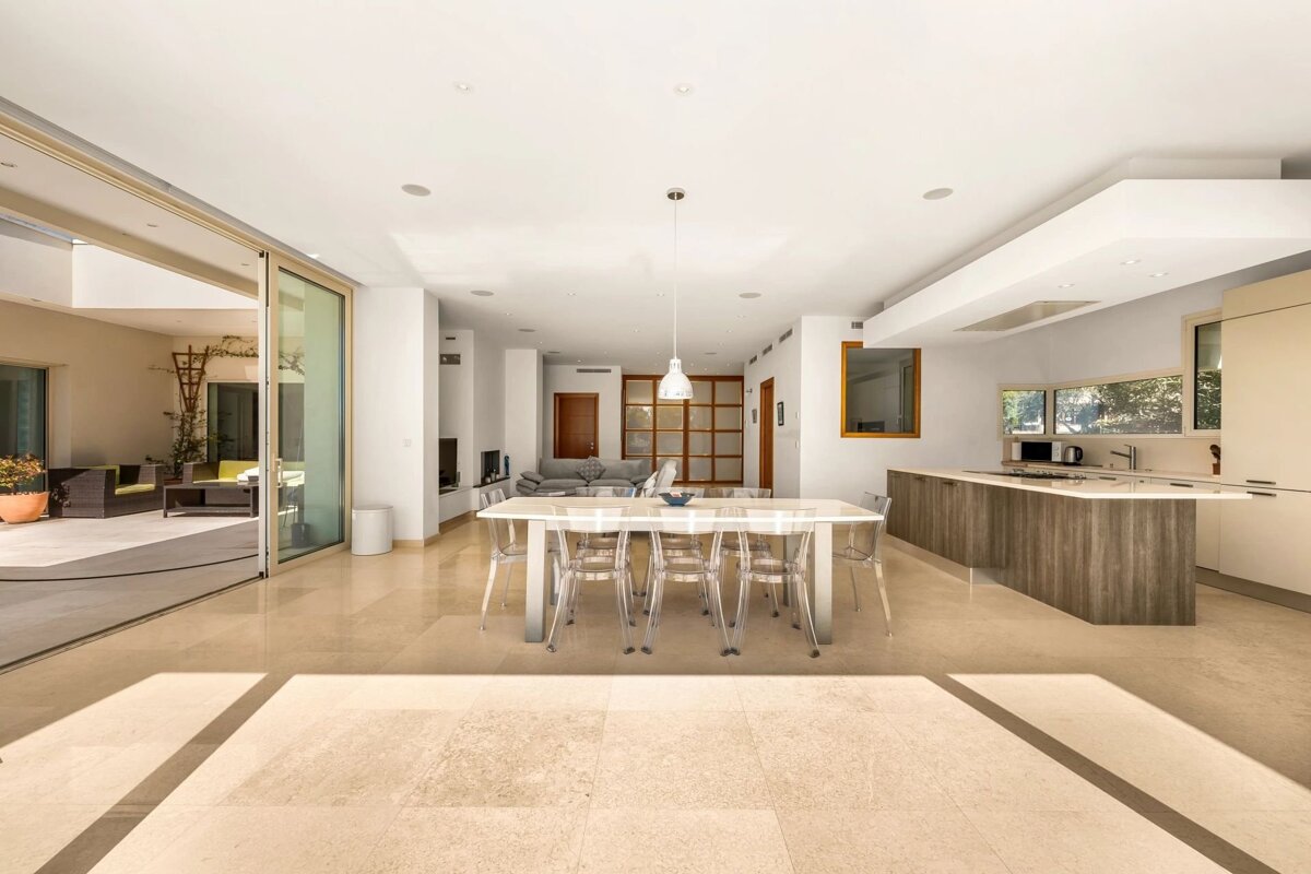 Bright modern open-concept dining and kitchen space featuring transparent chairs and large sliding glass doors opening to an outdoor patio.